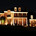 House lit up at night with very nice exterior lighting... starry sky and slight glow highlight the rooftop.